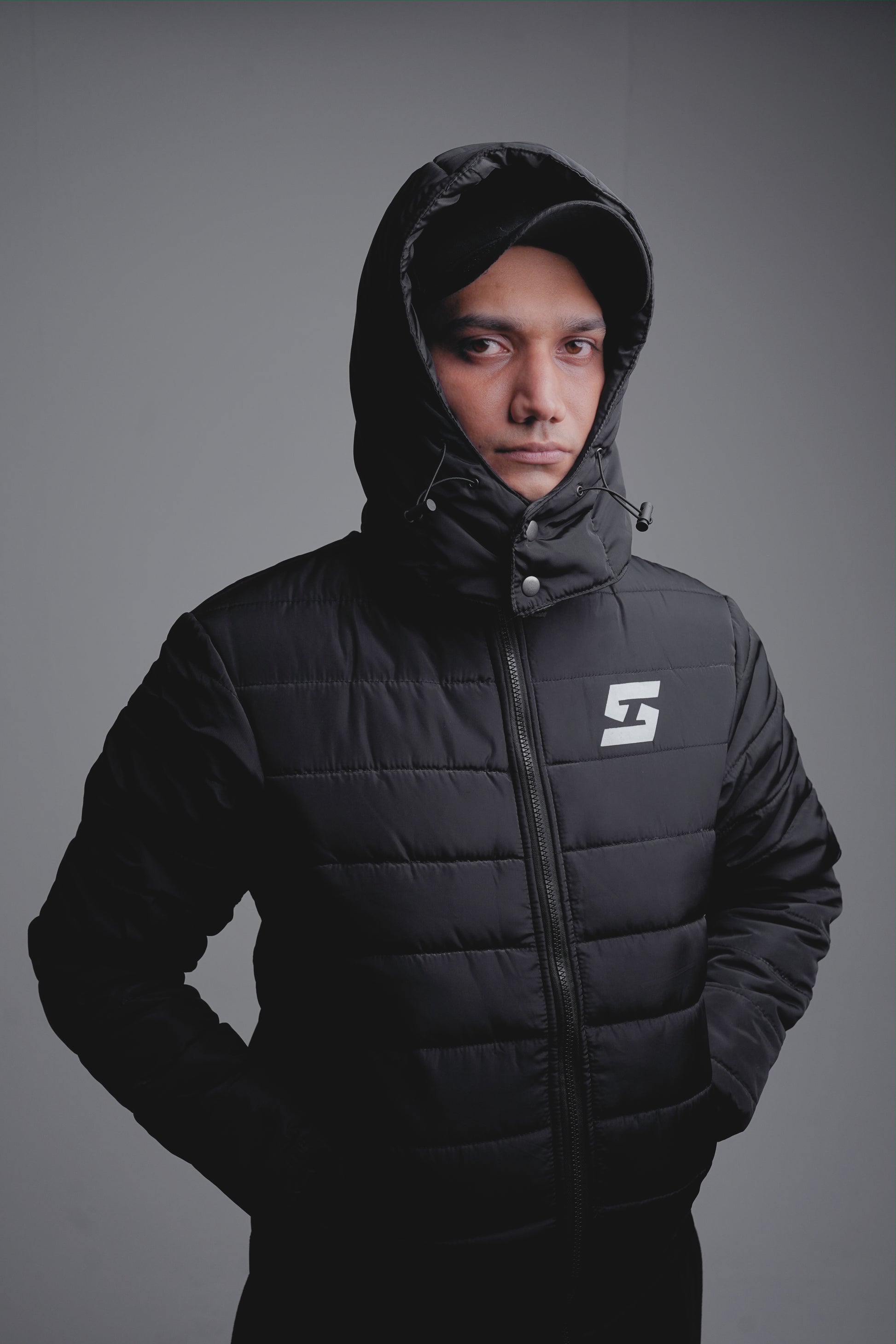 Man wearing black winter hooded jacket with down insulation and zipper closure, showcasing street fashion style.