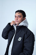 Man wearing a black winter hooded jacket with a logo, showcasing street fashion and cold-weather comfort.