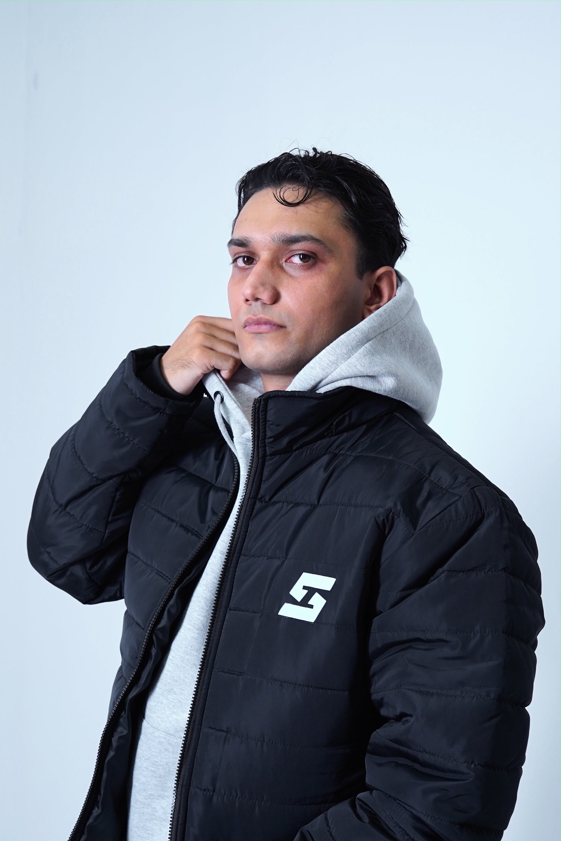 Man wearing a black winter hooded jacket with a logo, showcasing street fashion and cold-weather comfort.