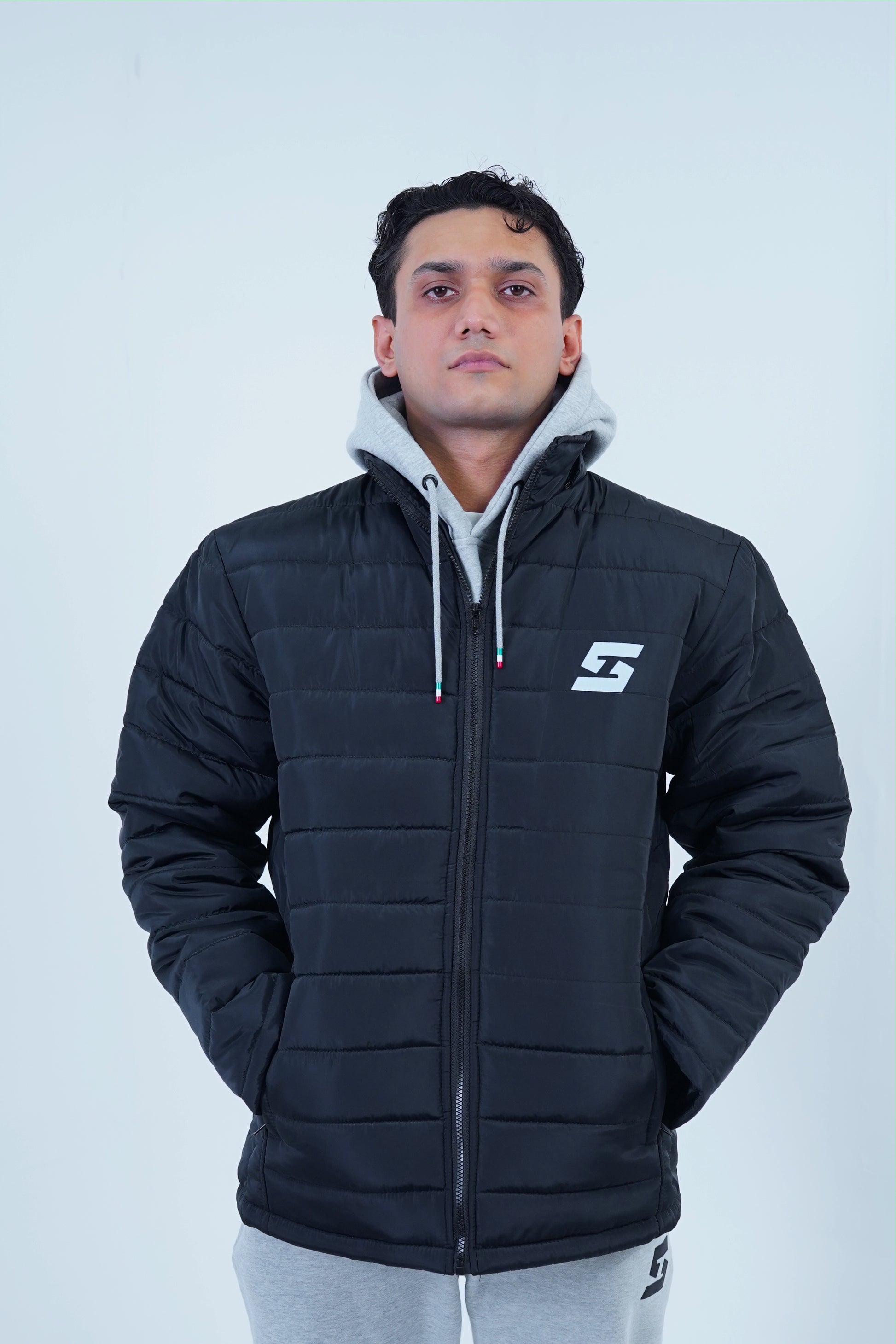 Man wearing a black hooded winter jacket with branded logo, showcasing warm street fashion style.